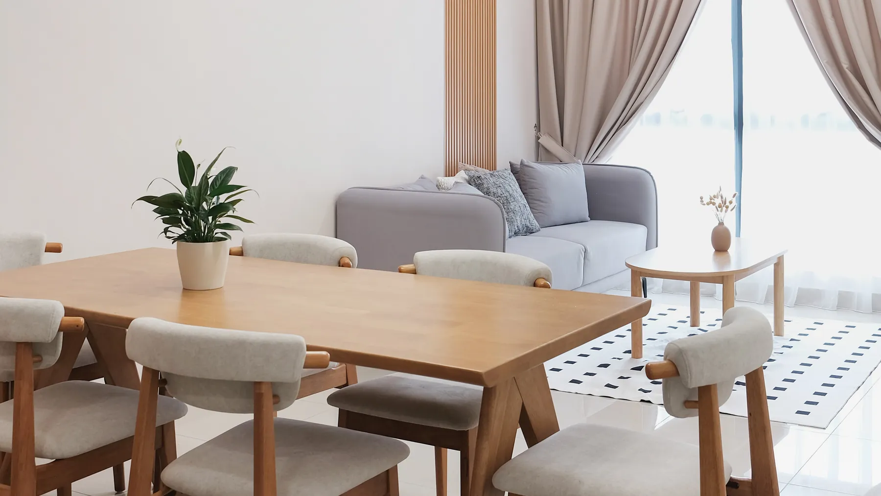 Bright living and dining room with a wooden table, upholstered chairs and a grey sofa