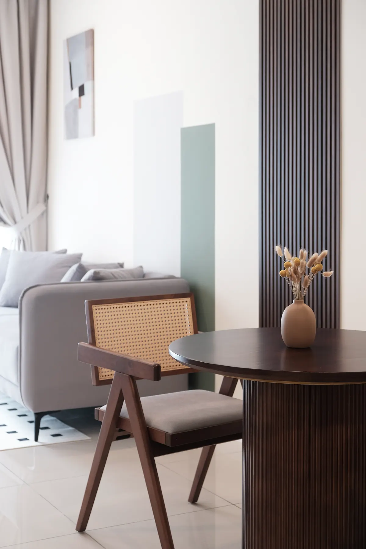 Dining chair and round table beside a grey sofa in a bright living room